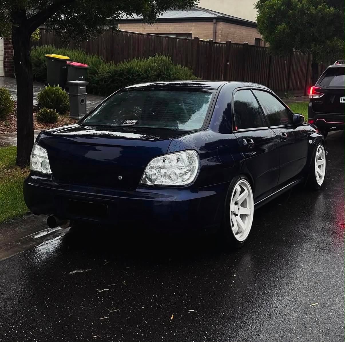 Navy Subaru Impreza sedan on a wet suburban street showing clear rear tail lights