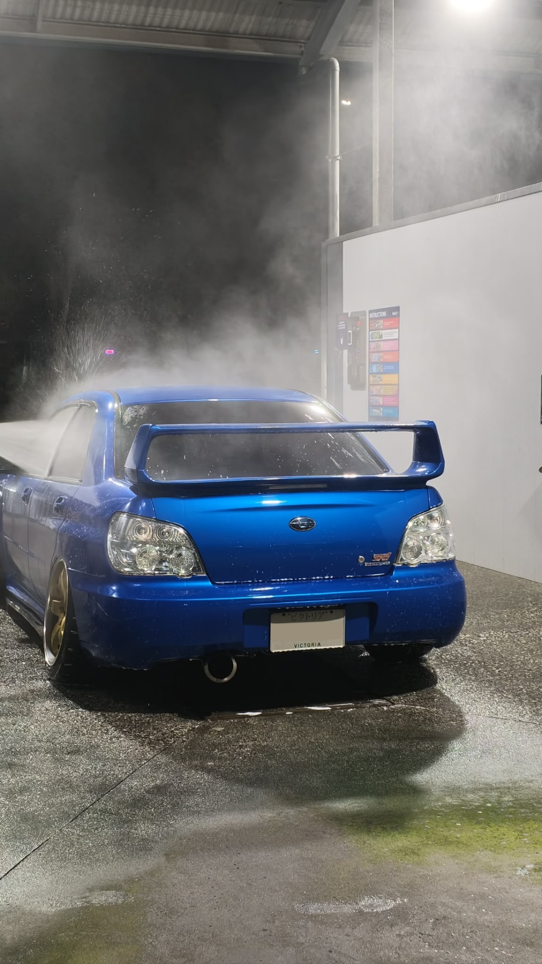 Blue Subaru Impreza sedan at a car wash at night, clear tail lights and headlights visible